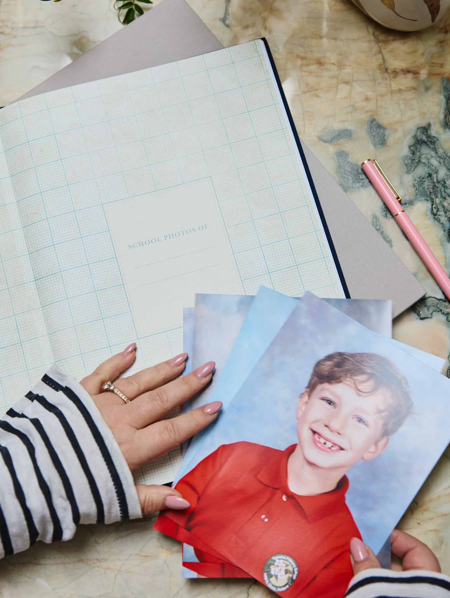 School Photos journal with pink hardcover and gold foil title, lying flat on a stone surface beside school photos and a cup of tea.