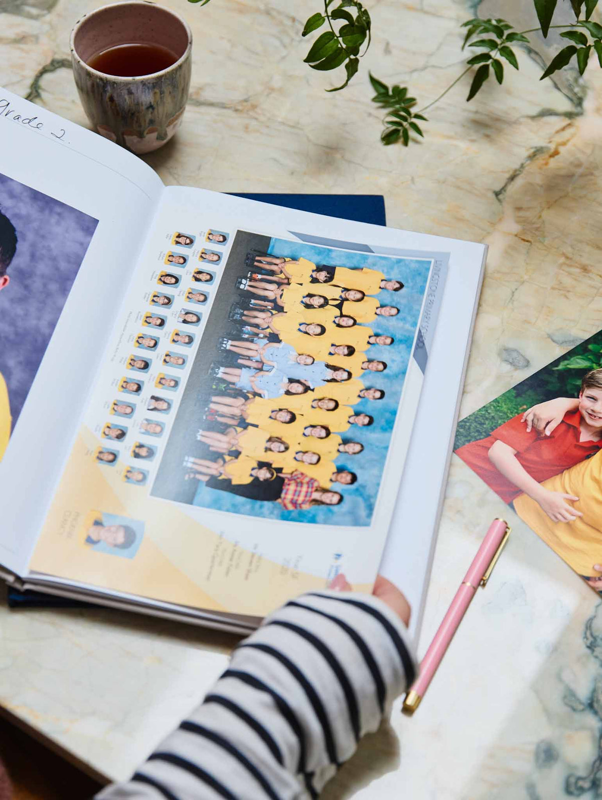 Open school journal with a class photo on a table with a hand holding a pen.