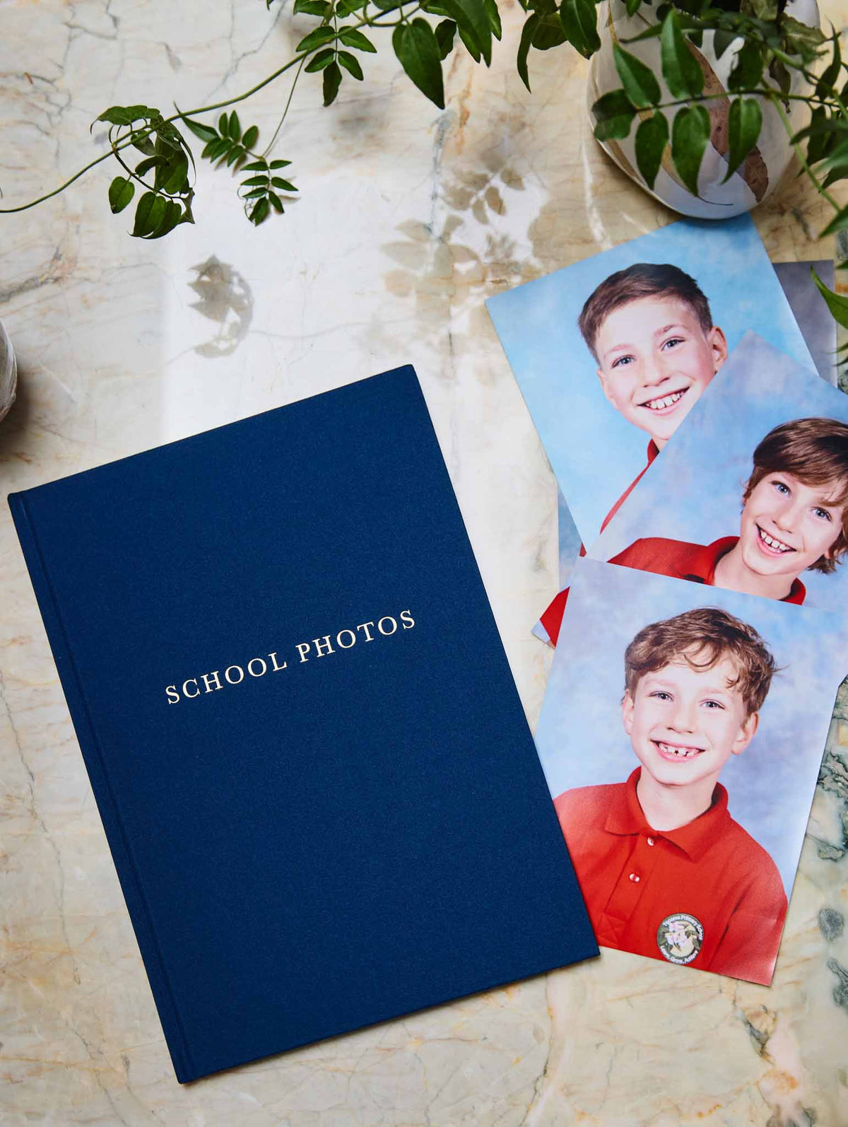 Navy &#39;School Photos&#39; album with three photos of a boy on a light stone surface.