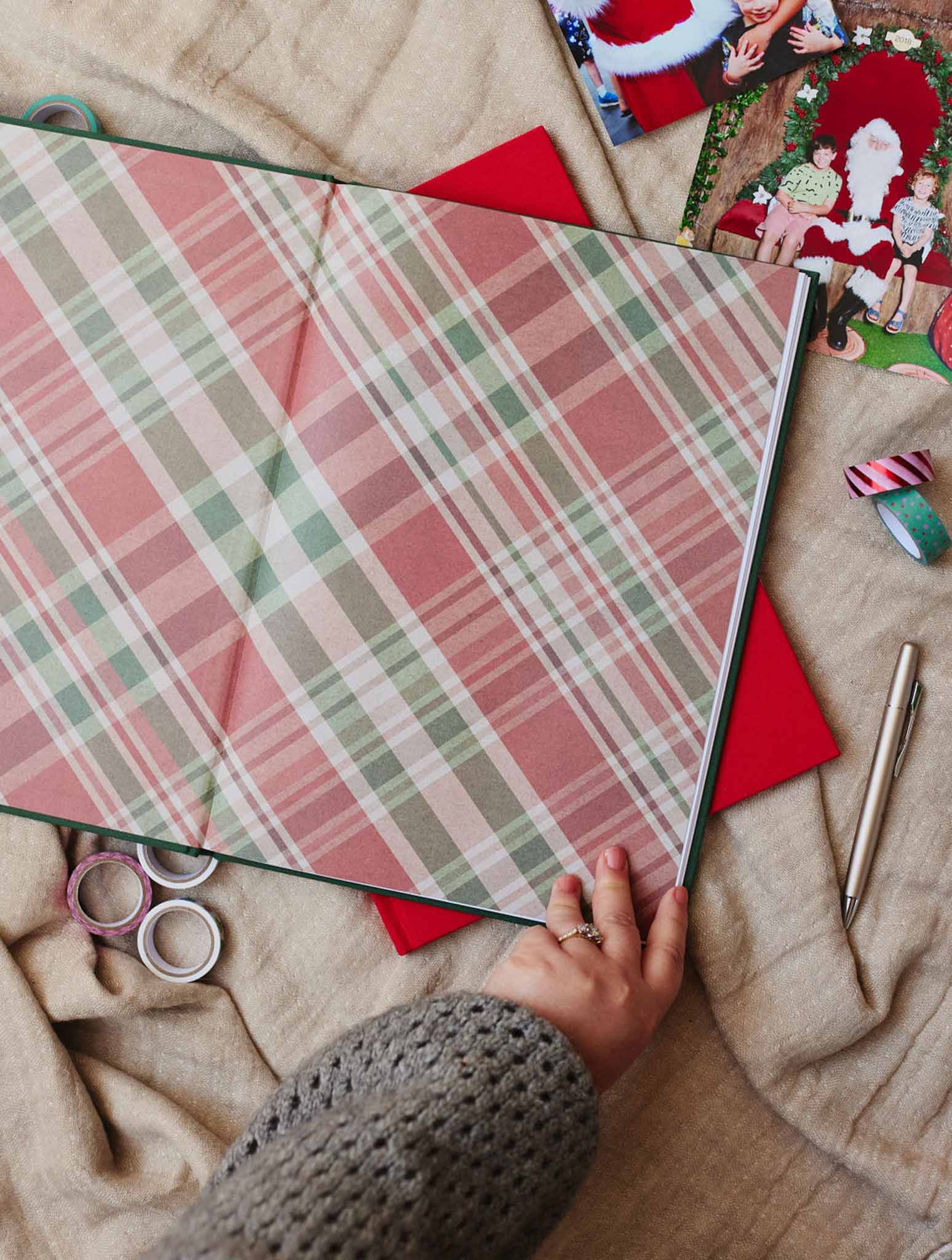 Christmas Photos journal with forest green hardcover and gold foil title, closed and lying flat on a linen surface beside a red cover variant, washi tape and loose Christmas photos.